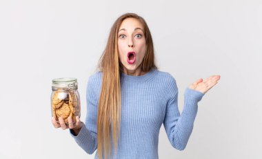 Zayıf, güzel bir kadın şaşırmış ve şok olmuş görünüyor. Çenesi düşmüş, elinde bir nesne, elinde kurabiyeyle.