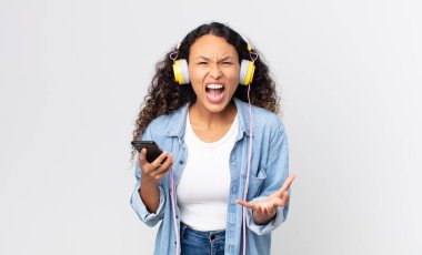 İspanyol güzel bir kadın kızgın, sinirli ve hayal kırıklığına uğramış görünüyor ve elinde akıllı telefon ve kulaklık tutuyor.