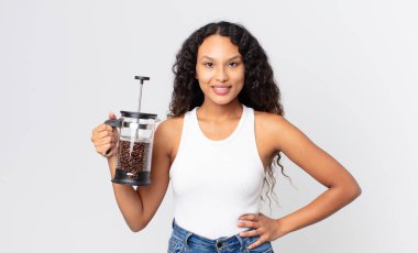 İspanyol güzel kadın mutlu bir şekilde gülümsüyor elleri kalçasında ve kendine güveni tam bir kahve makinesiyle.