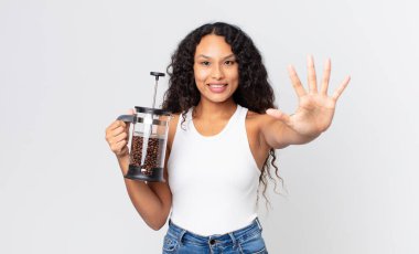 İspanyol güzel kadın gülümsüyor ve arkadaş canlısı görünüyor. Beş numarayı manuel kahve makinesiyle gösteriyor.