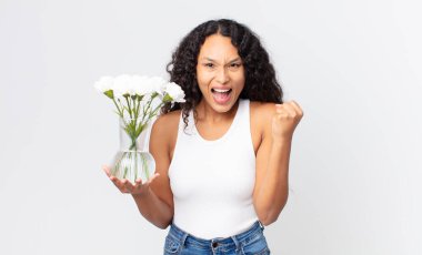 İspanyol güzel kadın şoke olmuş, gülüyor, başarıyı kutluyor ve elinde bir çiçek kavanozu tutuyor.