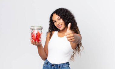 İspanyol güzel kadın gururlu, olumlu gülümsüyor başparmakları havada ve elinde kırmızı meyankökü jelibonuyla