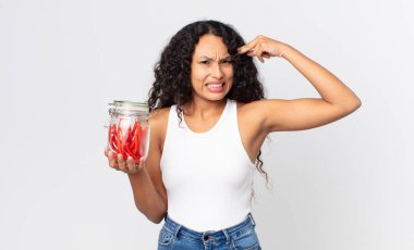 İspanyol güzel kadın şaşkın ve şaşkın hissediyor, deli olduğunu gösteriyor ve elinde kırmızı meyankökü jelibonu tutuyor.