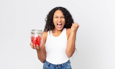 İspanyol güzel kadın kızgın bir ifadeyle agresif bir şekilde bağırıyor ve elinde kırmızı meyankökü şekeri tutuyor.