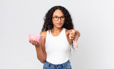 İspanyol asıllı güzel bir kadın kendini kötü hissediyor, baş parmağını kaldırıyor ve boş bir tencere tutuyor.