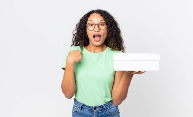 İspanyol güzel kadın mutlu hissediyor ve heyecanlı ve elinde beyaz bir kutuyla kendini işaret ediyor.