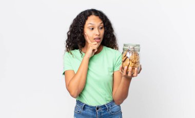 İspanyol güzel kadın mutlu bir şekilde gülümsüyor ve hayal kuruyor ya da şüphe ediyor ve elinde bir kurabiye şişesi tutuyor.