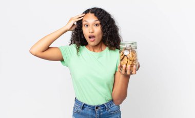 İspanyol güzel kadın mutlu, şaşkın ve şaşırmış görünüyor ve elinde bir kurabiye şişesi tutuyor.