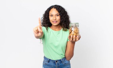 İspanyol güzel kadın gülümsüyor ve arkadaş canlısı görünüyor. Bir numarayı gösteriyor ve elinde bir kurabiye şişesi tutuyor.