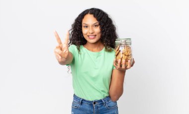 İspanyol güzel kadın gülümsüyor ve arkadaş canlısı görünüyor, ikinciyi gösteriyor ve elinde bir kurabiye şişesi tutuyor.