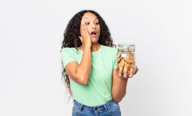 İspanyol güzel kadın mutlu, heyecanlı ve şaşırmış hissediyor ve elinde kurabiye şişesi tutuyor.