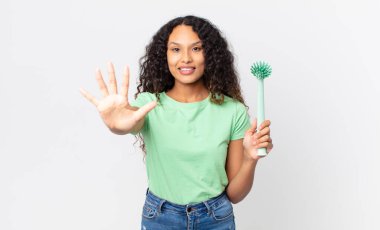 İspanyol güzel kadın gülümsüyor ve arkadaş canlısı görünüyor, beş numarayı gösteriyor ve elinde bulaşık fırçası var.