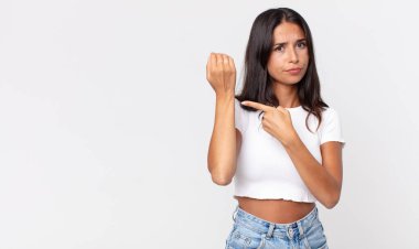 Oldukça zayıf İspanyol bir kadın sabırsız ve kızgın görünüyor, saati işaret ediyor.