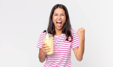 Kızgın bir ifadeyle bağıran ve elinde vanilyalı bir milkshake tutan genç İspanyol kadın.