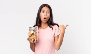 İnanamadığı için hayrete düşmüş ve elinde cam bir kurabiye şişesi tutan genç İspanyol kadın.