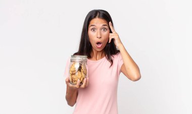 Genç İspanyol kadın şaşırmış görünüyor, yeni bir düşünce, fikir ya da konsept buluyor ve elinde cam bir kurabiye şişesi tutuyor.