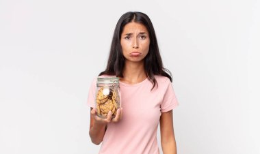 Genç İspanyol kadın üzgün ve mızmızlanıyor. Mutsuz bakıyor, ağlıyor ve elinde cam bir kurabiye şişesi tutuyor.