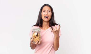 Genç İspanyol kadın umutsuz, sinirli ve stresli görünüyor ve elinde cam bir kurabiye şişesi tutuyor.