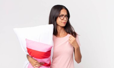 Genç İspanyol kadın kibirli, başarılı, pozitif ve gururlu görünüyor pijama giyiyor ve yastık tutuyor.