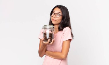 Genç İspanyol kadın omuz silkiyor, kafası karışık ve kararsız ve elinde kahve şişesi tutuyor.