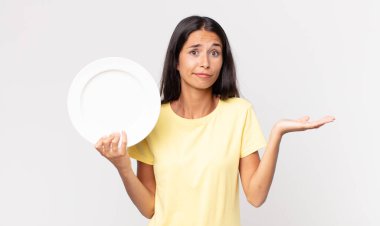 Genç İspanyol kadın şaşkın, şaşkın, şüpheci ve elinde boş bir tabak tutuyor.