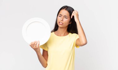 Genç İspanyol kadın şaşkın ve kafası karışmış hissediyor. Kafasını kaşıyor ve elinde boş bir tabak tutuyor.