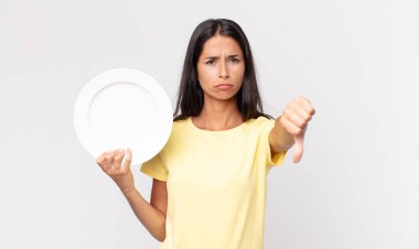 Genç İspanyol kadın kendini kötü hissediyor, baş parmağını kaldırıyor ve boş bir tabak tutuyor.