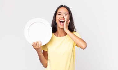 Genç İspanyol kadın kendini mutlu hissediyor, elleri ağızının yanında ve boş bir tabağı tutarak bağırıyor.