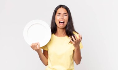 Genç İspanyol kadın umutsuz, sinirli ve stresli görünüyor ve elinde boş bir tabak tutuyor.