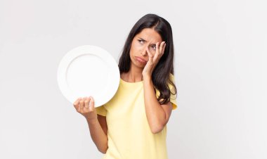 Genç İspanyol bir kadın yorgun ve uykulu bir şekilde sıkılmış, hayal kırıklığına uğramış ve boş bir tabak tutuyor.