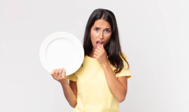 Ağzı ve gözleri sonuna kadar açık, eli çenesinde ve elinde boş bir tabakla İspanyol genç bir kadın.