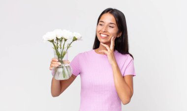 Genç İspanyol kadın mutlu bir şekilde gülümsüyor ve hayal kuruyor ya da elinde dekoratif çiçekler tutuyor.