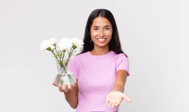 Genç İspanyol kadın mutlu bir şekilde gülümsüyor ve elinde dekoratif çiçekler tutan bir konsept sunuyor.