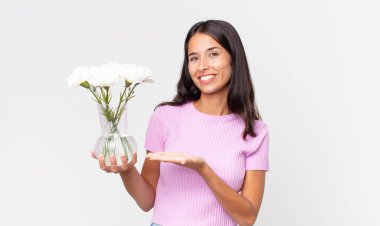 Genç İspanyol kadın neşeyle gülümsüyor, mutlu hissediyor ve elinde dekoratif çiçekler tutan bir konsept gösteriyor.