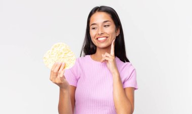 Genç İspanyol kadın mutlu bir şekilde gülümsüyor ve hayal kuruyor ya da kuşkulanıyor ve elinde pirinç kurabiyesi tutuyor. diyet kavramı