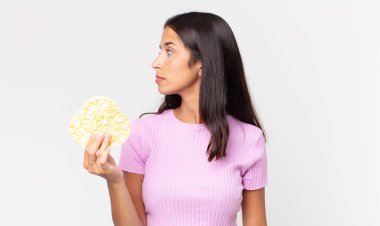 Profil görünümlü genç İspanyol kadın hayal kuruyor ya da hayal kuruyor ve elinde pirinç kurabiyesi tutuyor. diyet kavramı