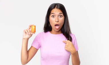 Genç İspanyol kadın şok olmuş ve şaşırmış görünüyor ağzı sonuna kadar açık, kendini işaret ediyor ve elinde pil tutuyor.