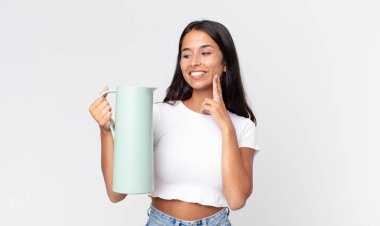 Genç İspanyol kadın mutlu bir şekilde gülümsüyor ve hayal kuruyor ya da şüphe ediyor ve elinde kahve termosu tutuyor.