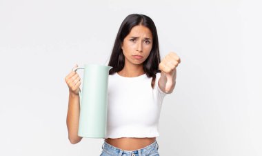 Genç İspanyol kadın kızgın hissediyor, baş parmaklarını gösteriyor ve elinde kahve termosu tutuyor.