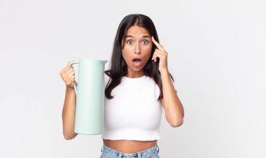 Genç İspanyol kadın şaşırmış görünüyor, yeni bir düşünce, fikir ya da konsept buluyor ve elinde kahve termosu tutuyor.