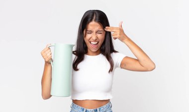 Genç İspanyol kadın mutsuz ve stresli görünüyor, intihar jesti silah işareti yapıyor ve elinde kahve termosu tutuyor.