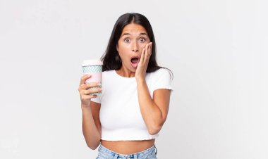 Genç İspanyol kadın şok olmuş ve korkmuş hissediyor ve elinde bir kahve kabı tutuyor.