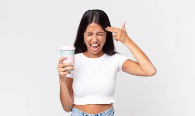 Genç İspanyol kadın mutsuz ve stresli görünüyor, intihar jesti silah işareti yapıyor ve elinde kahve kabı tutuyor.