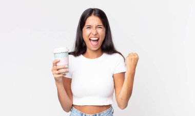 Genç İspanyol kadın kızgın bir ifadeyle agresif bir şekilde bağırıyor ve elinde bir kahve kabı tutuyor.