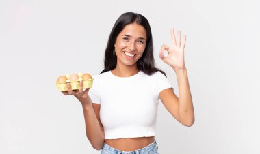 Genç İspanyol kadın kendini mutlu hissediyor. Onaylıyor. Güzel bir jest yapıyor ve elinde bir yumurta kutusu tutuyor.