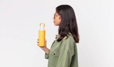 Profilde Latin kökenli genç bir kadın hayal kuruyor, hayal kuruyor ve elinde kahve termosu tutuyor.