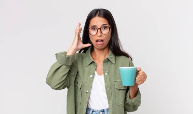 Elleri havada bağıran ve elinde kahve fincanı tutan genç İspanyol kadın.