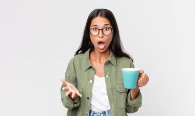 Genç İspanyol kadın şok olmuş, şaşırmış ve elinde kahve fincanı tutuyor.