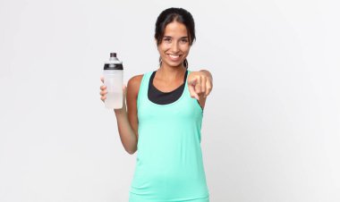 Genç İspanyol kadın kamerayı işaret ederek seni seçiyor ve elinde bir su şişesi tutuyor. fitness konsepti