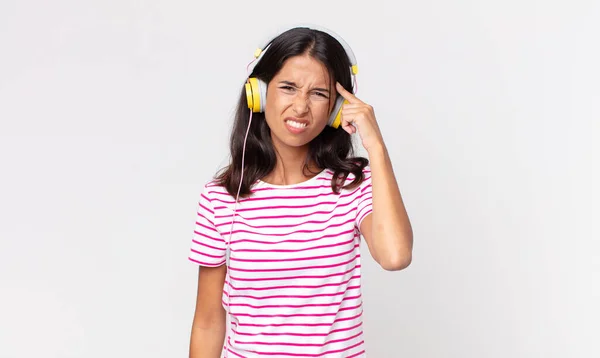 若いヒスパニック系の女性は混乱して困惑していますヘッドフォンで音楽を聴いています — ストック写真